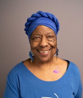 Smiling person wearing a blue turban and top, and long blue earrings.